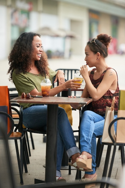 Beautiful stylish women sharing sweet delicious cocltails when meeting at outdoor cafe