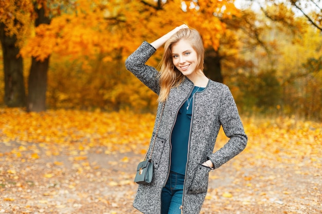 Beautiful stylish young woman with a smile in autumn clothes near trees with yellow foliage