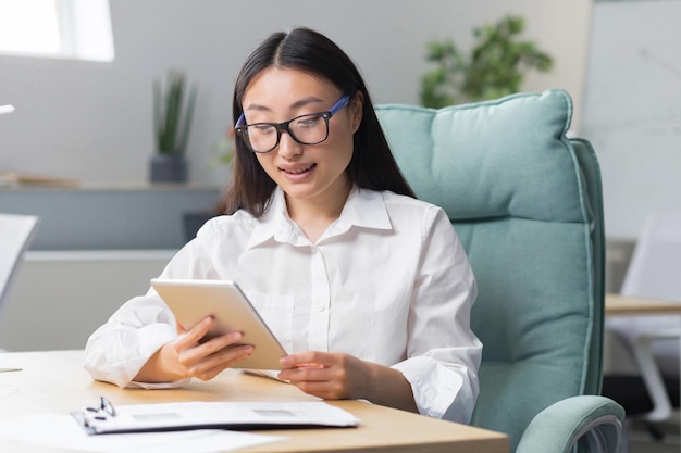 A beautiful and successful business woman works in a modern office an asian woman uses a tablet comp