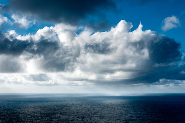 On a beautiful sunny day gray white and black clouds are playing over the sea where rain is falling