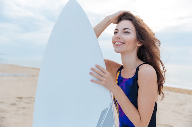 Beautiful surfer teen girl standing with surfboard at the beach