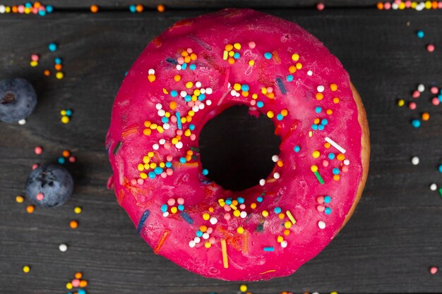 Photo beautiful sweet food colorful pink donut with colored sprinkles on a wooden background