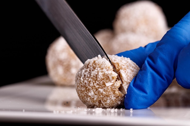 Beautiful sweets with coconut are cut with a knife on a white plate on a black background