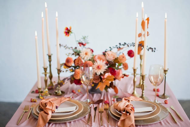 Beautiful table setting with autumn flowers orange and pink napkins and burning candles