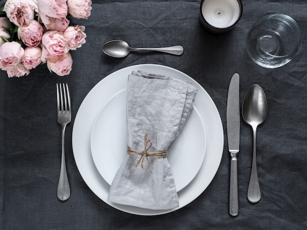 Beautiful table setting with pink spray roses and candle on gray linen tablecloth. 