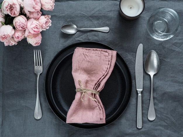 Beautiful table setting with pink spray roses and candle on gray linen tablecloth.