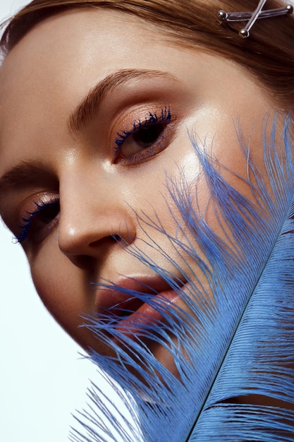 Beautiful tanned girl with creative makeup and blue eyelashes feather in hand Beauty face