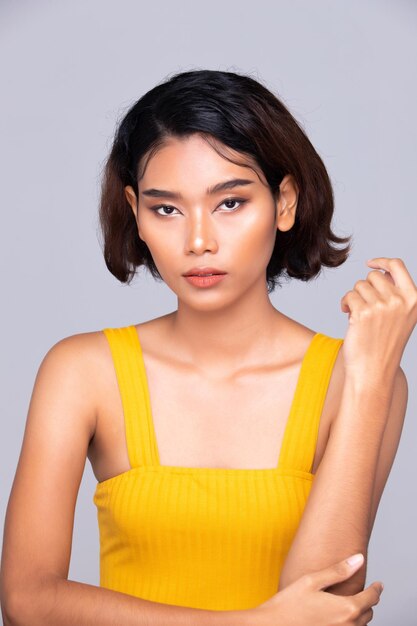 Beautiful Tanned skin woman wear yellow dress open shoulder with clean look make up and curl hair Portrait young girl in attractive natural fashion face express feel smile isolated gray background