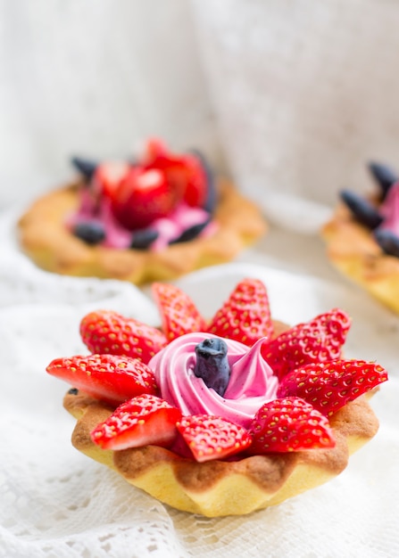 Beautiful tasty cupcakes close up with strawberries, honeysuckle and pink cream