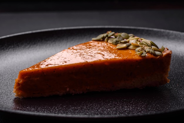 Beautiful tasty pumpkin pie with slices on a black ceramic plate on a dark concrete background