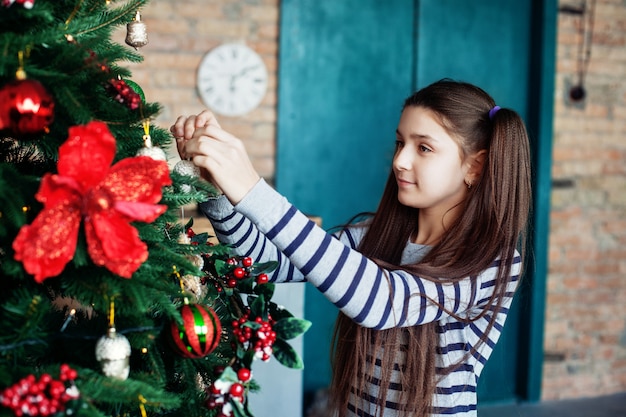 Beautiful teen girl decorates the Christmas tree in the house.