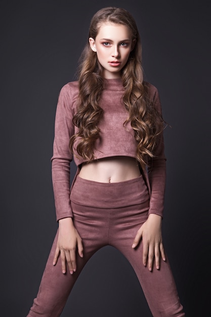 Beautiful teen girl with long wavy hair posing in the studio on a black background, dressed in a pink corduroy suit. Fashion concept