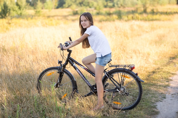 Beautiful teenage girl posing on bicycle in field at hot sunny day