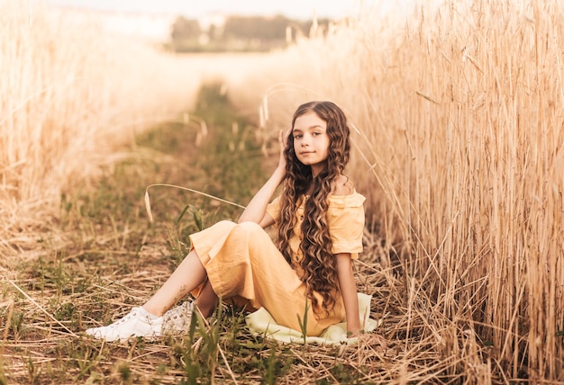 Beautiful teenage girl with long hair walking through a wheat field on a sunny day. Outdoors portrait. Schoolgirl relaxing