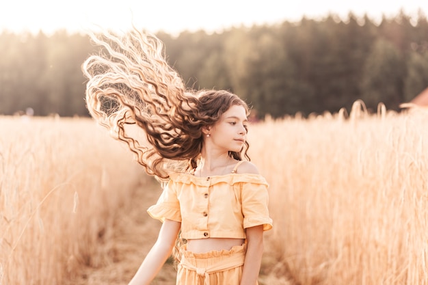 Beautiful teenage girl with long hair walking through a wheat field on a sunny day. Outdoors portrait. Schoolgirl relaxing