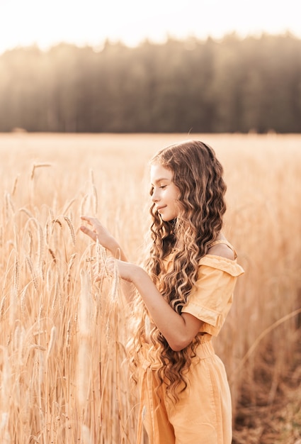 Beautiful teenage girl with long hair walking through a wheat field on a sunny day. Outdoors portrait. Schoolgirl relaxing