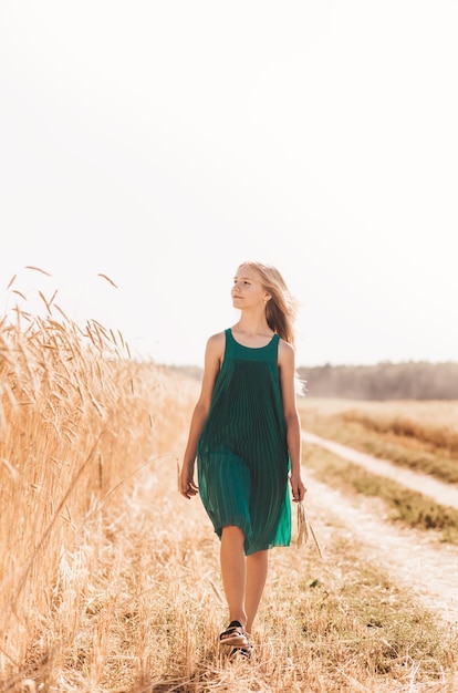 Beautiful teenage girl with long white hair walking through a wheat field on a sunny day