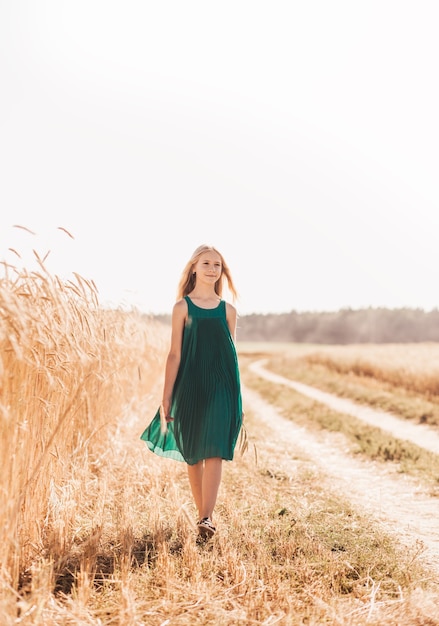 Beautiful teenage girl with long white hair walking through a wheat field on a sunny day