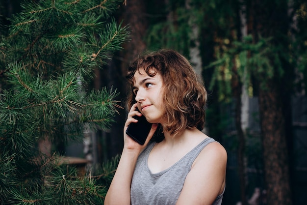 Beautiful teenager girl talking by phone at the forest. Using technology