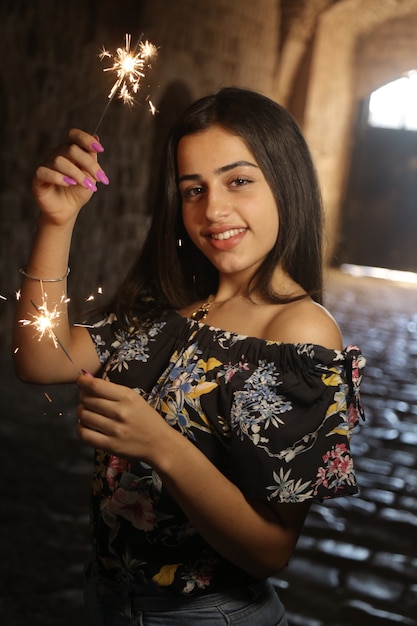 Beautiful teenager girl with fireworks candles light an field ancient castle summer background