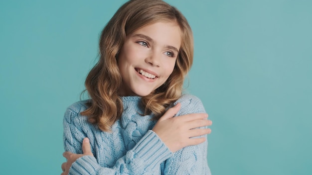 Beautiful tender blond teenage girl in knitted cozy sweater enjoying warm looking cute over blue background