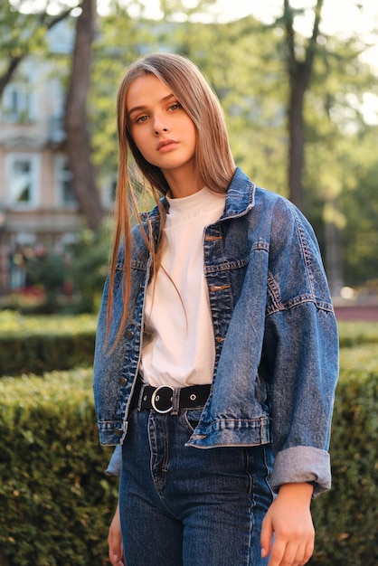 Beautiful thoughtful stylish brown haired girl in denim jacket confidently looking in camera outdoor