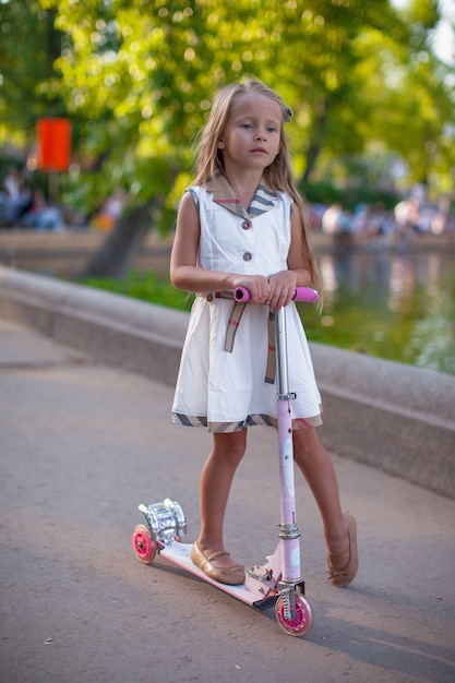 Beautiful toddler girlin dress on the scooter in a park