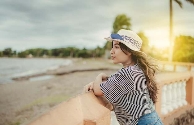 Beautiful tourist girl in hat looking at the beach from a pier Portrait of female traveler on a pier looking at the horizon