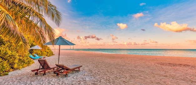 Beautiful tropical sunset beach. Romantic couple goals two sun beds, umbrella under palm tree leaves