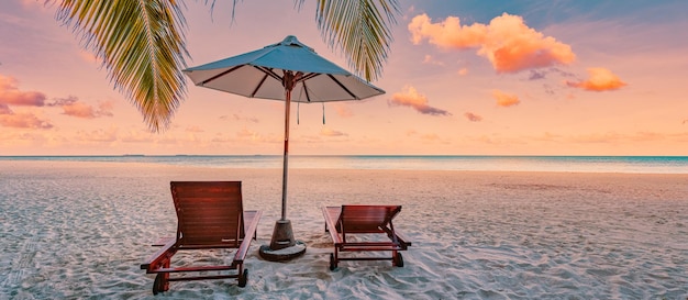 Beautiful tropical sunset beach. Romantic couple goals, two sun beds umbrella under palm tree leaves