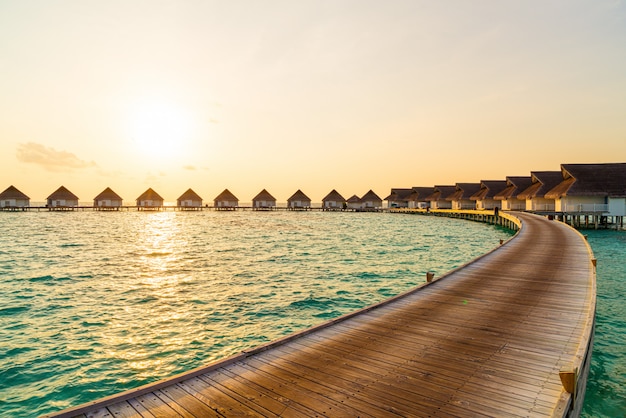 Beautiful tropical sunset over Maldives island with water bungalow in hotel resort