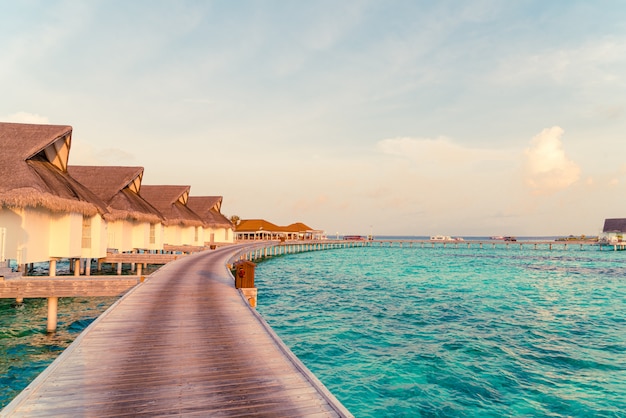 Beautiful tropical sunset over Maldives island with water bungalow in hotel resort