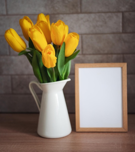 Beautiful tulip flowers and blank picture frame on table at kitchen