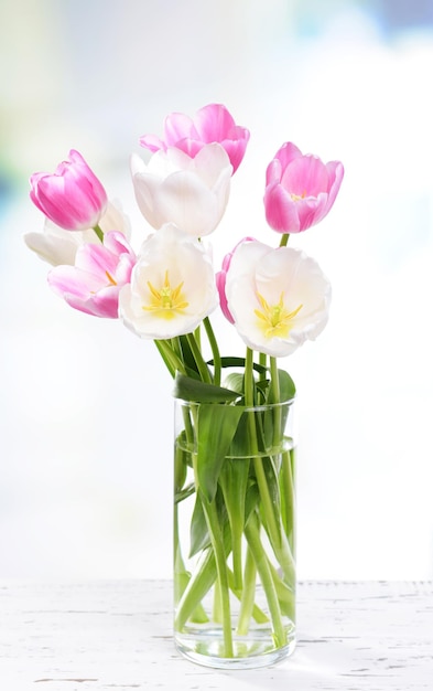 Beautiful tulips in bucket in vase on table on light background