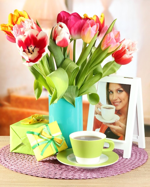 Beautiful tulips in bucket with gifts and cup of tea on table in room