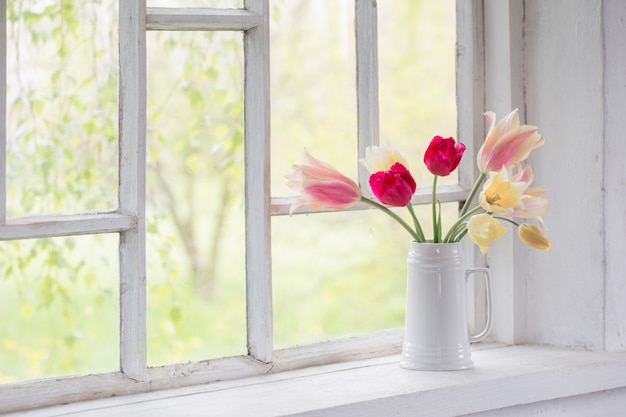 Beautiful tulips in vase on white windowsill