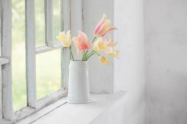 Beautiful tulips in vase on white windowsill