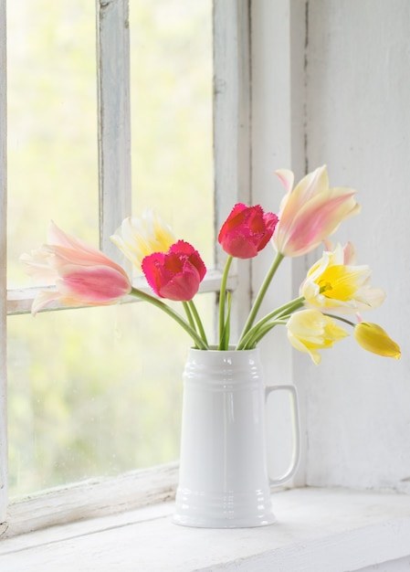 Beautiful tulips in vase on white windowsill