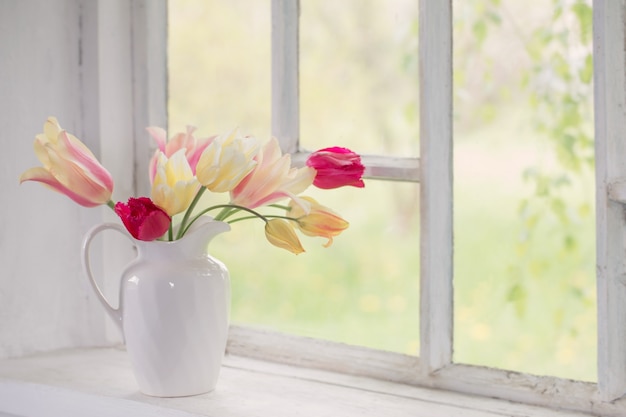 Beautiful tulips in vase on white windowsill