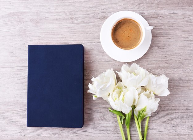 Photo beautiful tulips with diary and cup of coffee on wooden table top view