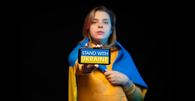 Photo beautiful ukrainian girl with a state flag and smartphone in hands with a call stand with ukraine the actual concept of antiwar support russianukrainian war prays for ukraine stop war