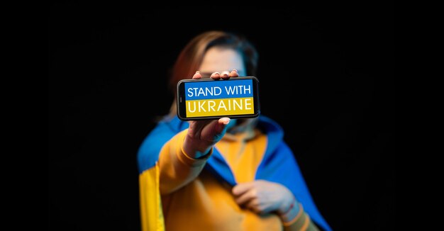 Photo beautiful ukrainian girl with a state flag and smartphone in hands with a call stand with ukraine the actual concept of antiwar support russianukrainian war prays for ukraine stop war