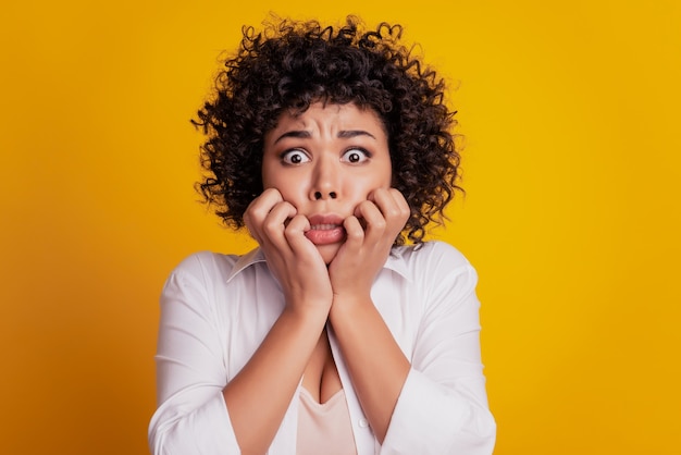 Beautiful unhappy girl bite gnaw nails look terrified camera posing on yellow background