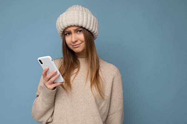 beautiful upset young blonde woman wearing stylish beige warm sweater and knitted winter