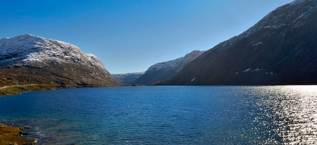 Beautiful view of a blue water in a fjord in norway with snowcapped mountains under blue sky