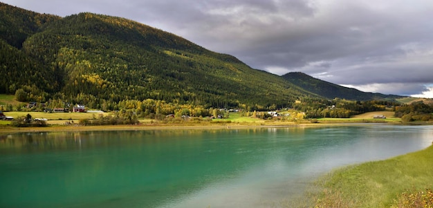 Beautiful view on sea water in norway with green hills and village under cloudy sky