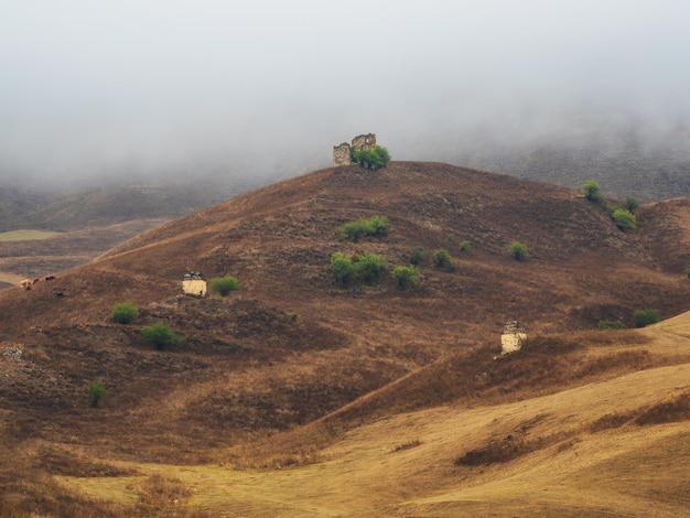 Beautiful views of Ingushetia Old crypts on misty autumn slopes Misty morning in the Caucasus mountains Medieval tower on foggy mountain slope background