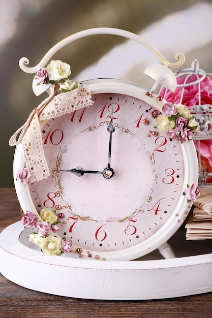 Beautiful vintage alarm clock with flowers on light background