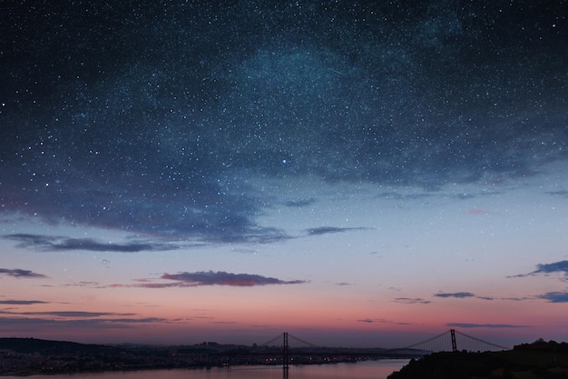 Beautiful vintage city of Lisbon with river bridge and colorful sunset evening sky with stars Amazing starry sky Space wallpaper