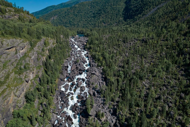 A beautiful waterfall flowing through the rocky hills with many different trees under a blue cloudless sky.